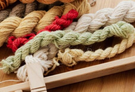 Yarn Tools - From above of unfinished tapestry on manual wooden loom placed on wooden table with assorted yarn twists and wooden needles during weaving process in workshop