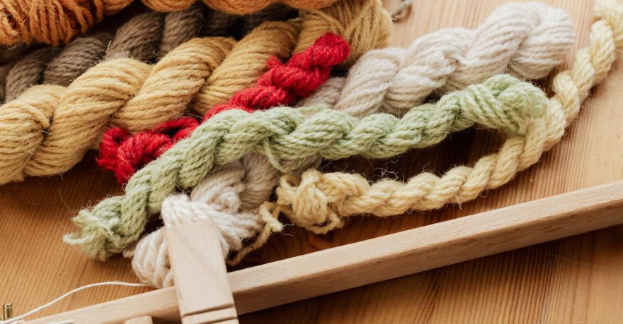 Yarn Tools - From above of unfinished tapestry on manual wooden loom placed on wooden table with assorted yarn twists and wooden needles during weaving process in workshop