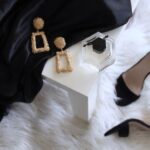 Luxury Yarn - pair of gold-colored earrings on table and black ankle-strap pumps on area rug