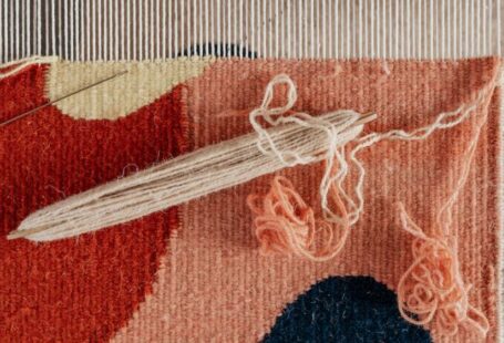 Yarn Tools - From above of shuttle and needle placed on part of handmade carpet with circle pattern on loom frame during weaving process