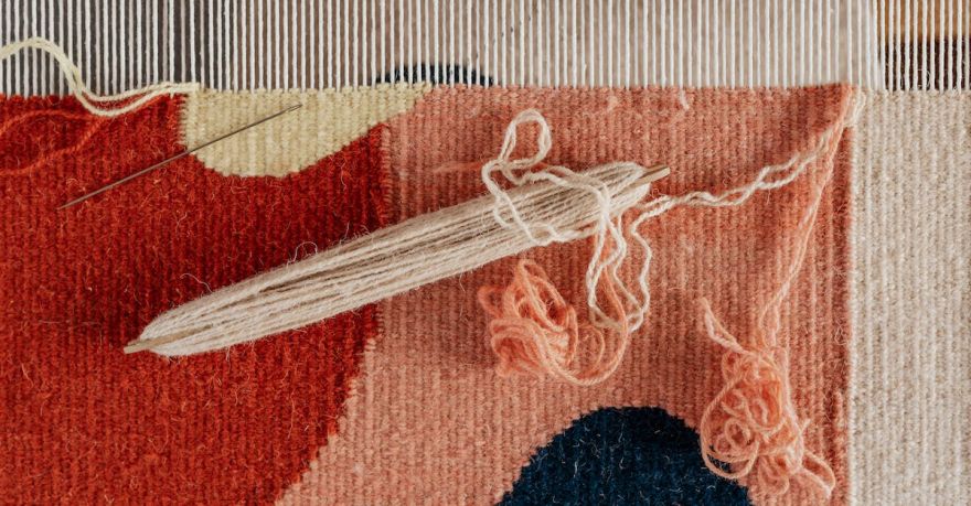 Yarn Tools - From above of shuttle and needle placed on part of handmade carpet with circle pattern on loom frame during weaving process