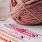 Yarn Tools - Closeup of row of multicolored crochet needles and ball of beige threads for knitting in bright room